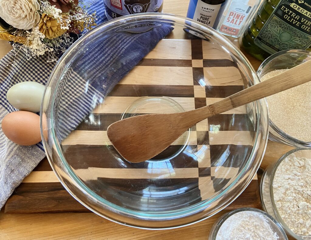 Empty glass mixing bowl for brownie batter and wooden spoon on a cutting board